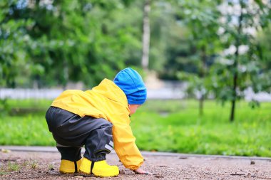 Sarı yağmurluklu çocuk, bak, sonbahar mevsimi parkta yürüyor.