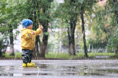 Yağmur yürüyüşü çocuk, sonbaharda parkta yağmur damlaları ve su birikintileri çocuk