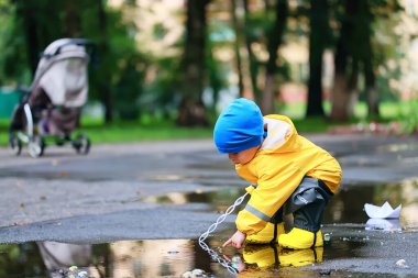 Su birikintilerinde dışarıda oynayan çocuk, sonbahar çocukluğunda lastik ayakkabılar, sarı yağmurluklar.