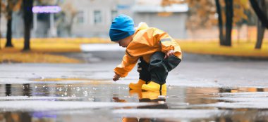 Su birikintilerinde dışarıda oynayan çocuk, sonbahar çocukluğunda lastik ayakkabılar, sarı yağmurluklar.