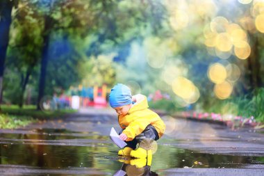 Kağıt tekne su birikintisi oyunu, erkek sezonu sonbahar yağmurluğu, sarı lastik çizmeler, açık hava oyunu