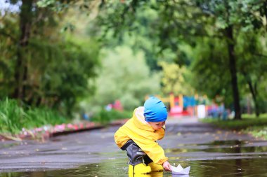 Kağıt tekne su birikintisi oyunu, erkek sezonu sonbahar yağmurluğu, sarı lastik çizmeler, açık hava oyunu