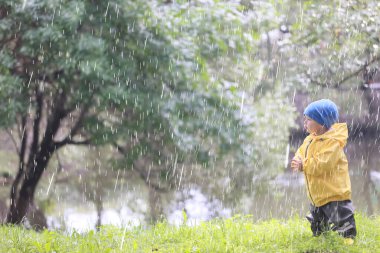 Yağmur yürüyüşü çocuk, sonbaharda parkta yağmur damlaları ve su birikintileri çocuk