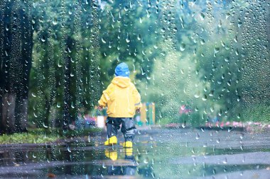 Yağmur yürüyüşü çocuk, sonbaharda parkta yağmur damlaları ve su birikintileri çocuk