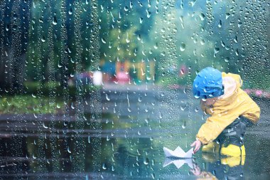Yağmur yürüyüşü çocuk, sonbaharda parkta yağmur damlaları ve su birikintileri çocuk