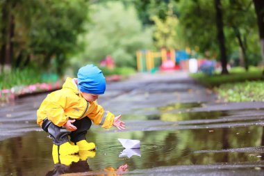Kağıt tekne su birikintisi oyunu, erkek sezonu sonbahar yağmurluğu, sarı lastik çizmeler, açık hava oyunu