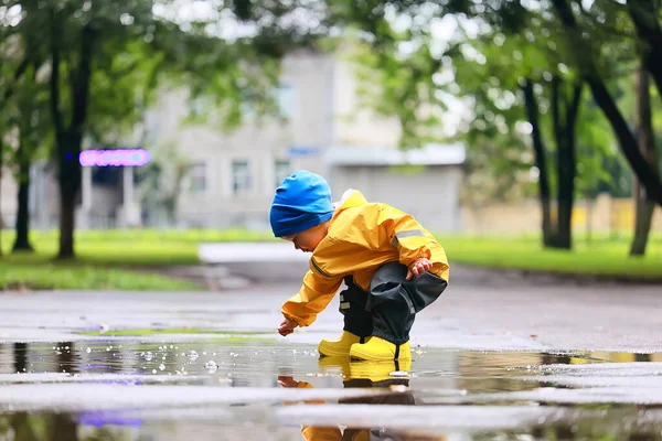 水たまりで屋外で遊ぶ男の子 秋の子供時代のゴム製の靴レインコート黄色 — ストック写真