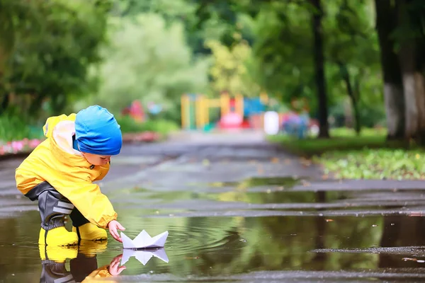 紙のボートの水たまりゲーム 男の子の季節の秋の外観のレインコート 黄色のゴム製のブーツ 屋外ゲーム — ストック写真