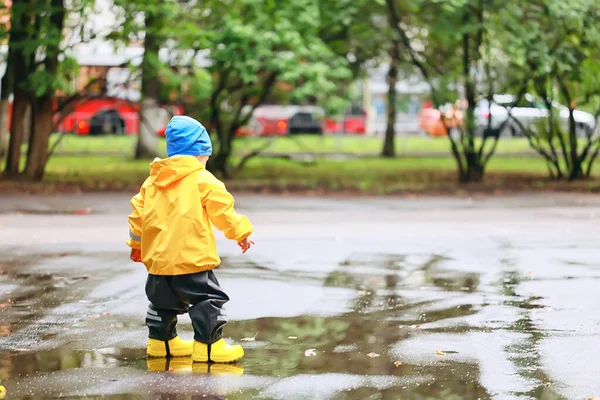 水たまりで屋外で遊ぶ男の子 秋の子供時代のゴム製の靴レインコート黄色 — ストック写真