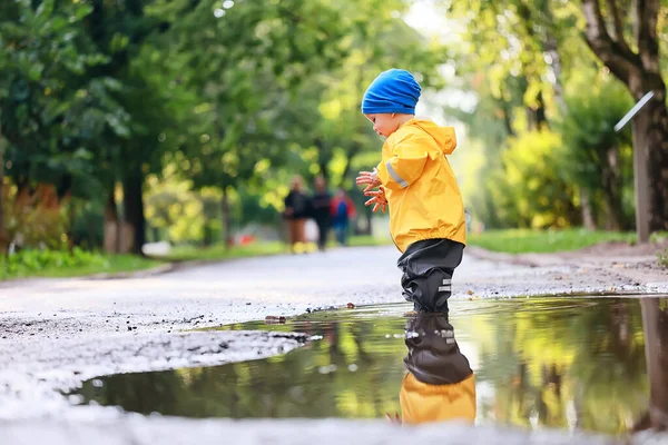 水たまりで屋外で遊ぶ男の子 秋の子供時代のゴム製の靴レインコート黄色 — ストック写真