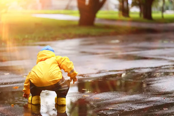 boy playing outdoors in puddles, autumn childhood rubber shoes raincoat yellow