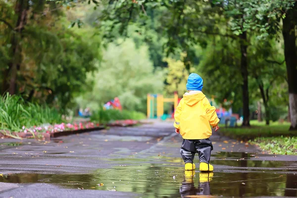 Su birikintilerinde dışarıda oynayan çocuk, sonbahar çocukluğunda lastik ayakkabılar, sarı yağmurluklar.