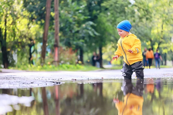 boy playing outdoors in puddles, autumn childhood rubber shoes raincoat yellow