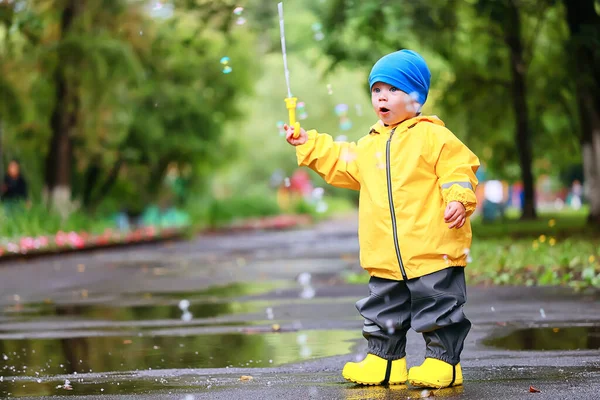 水たまりで屋外で遊ぶ男の子 秋の子供時代のゴム製の靴レインコート黄色 — ストック写真