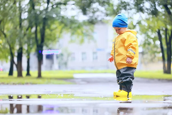 水たまりで屋外で遊ぶ男の子 秋の子供時代のゴム製の靴レインコート黄色 — ストック写真