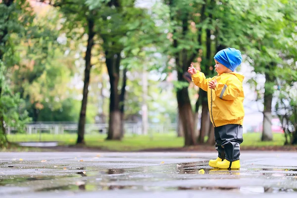 水たまりで屋外で遊ぶ男の子 秋の子供時代のゴム製の靴レインコート黄色 — ストック写真