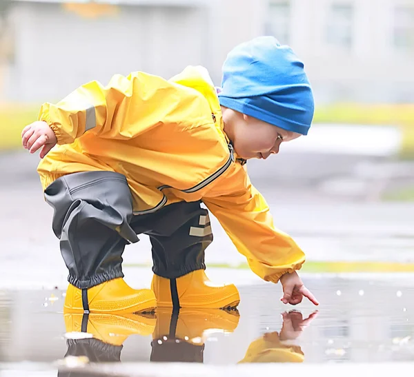 男孩在外面的水坑里玩耍 秋天的童年时代皮鞋黄色雨衣 — 图库照片