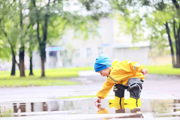 水たまりで屋外で遊ぶ男の子 秋の子供時代のゴム製の靴レインコート黄色 — ストック写真