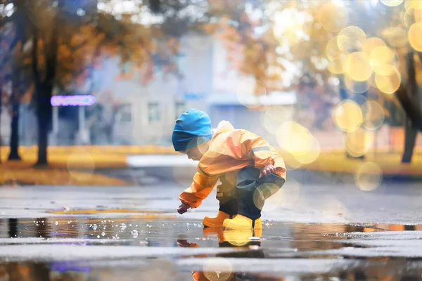 Su birikintilerinde dışarıda oynayan çocuk, sonbahar çocukluğunda lastik ayakkabılar, sarı yağmurluklar.