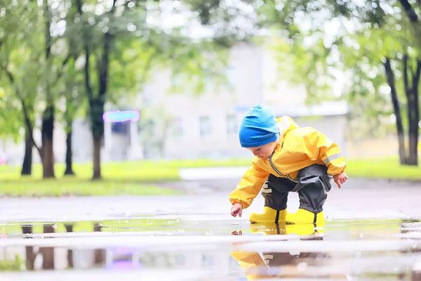 水たまりで屋外で遊ぶ男の子 秋の子供時代のゴム製の靴レインコート黄色 — ストック写真