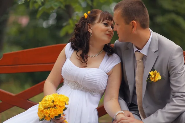 Bride and groom sitting on bench — Stock Photo, Image