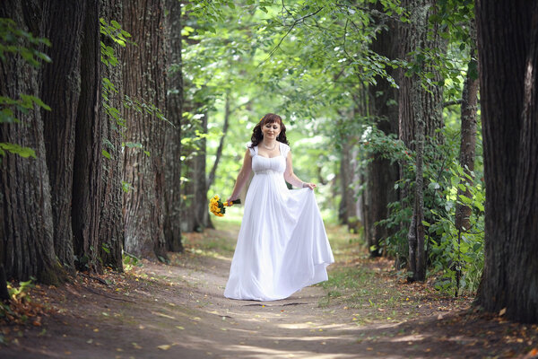 Wedding photo of bride walking in park in summer