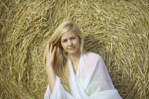 Blonde vrouw zitten in de buurt van het hooi — Stockfoto