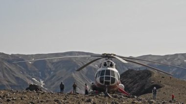 Helikopter ve insanlar açık havada Kamçatka dağlarının arka planında seyahat ediyorlar..