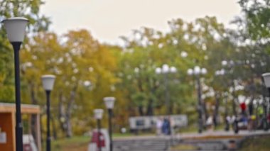 Şehir parkının bulanık manzarası ve sonbahar günü yürüyen gençler..