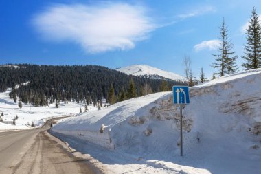 Güneşli bir günde, Sibirya, Rusya 'daki Batı Sayan dağlarında temiz yollu kış manzarası. Derin kar yığınlarının arasında asfalt yol sarar