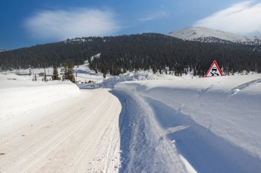 Güneşli bir günde dağ yolu. Kış sürüşü, karlı otoyolda. Yol kenarındaki yol işaretleri derin kar yığınlarıyla kaplı. Batı Sayan dağları, Sibirya, Rusya.