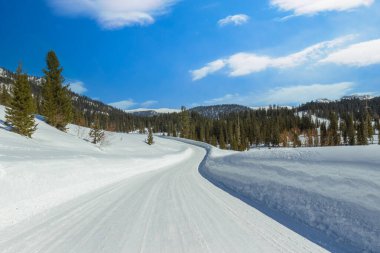 Kış dağlarında karlı bir yol. Güneşli bir günde Ergaki sıradağları, Batı Sayan Dağları, Sibirya, Rusya. Kış karlı yolda ilerliyor.
