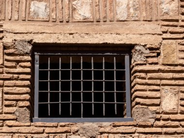 Taş duvarda paslı demir parmaklıklar olan pencere.