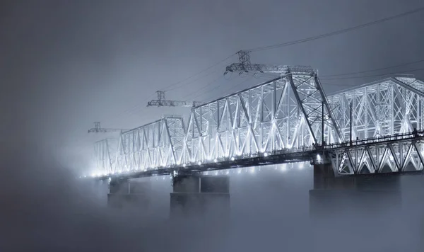 Glowing bridge hidden in the thick fog. Winter night on Yenisei river, Siberia