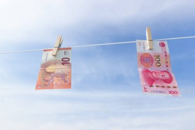 China Yuan ve Euro banknotları gökyüzüne karşı ahşap mandallara asılı..