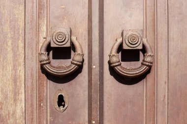 Büyük halkalar ve anahtar deliği şeklinde kapı kollarıyla kahverengi boyayla boyanmış eski ağır ahşap kapı..