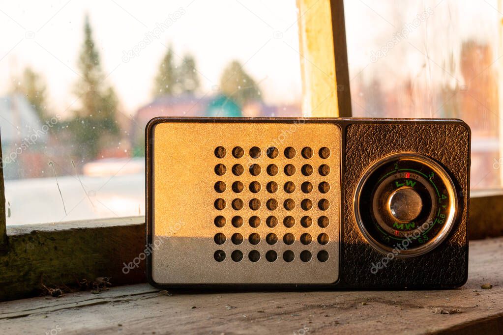 Vintage portable radio receiver stands on a dusty windowsill against the background of an unwashed window