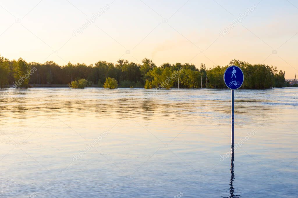 A road sign sticking out of the water during a flood. Flooded city embankment in Krasnoyarsk, Russia. Natural disaster