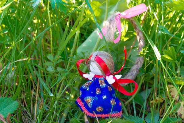 Dolyushka is a homemade amulet doll with a long curled top braid against green grass. Traditional folk doll made of fabric for family happiness and defender home.