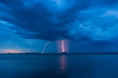 Suyun üzerindeki bir fırtına sırasında parlayan parlak yıldırımlarla dolu akşam manzarası