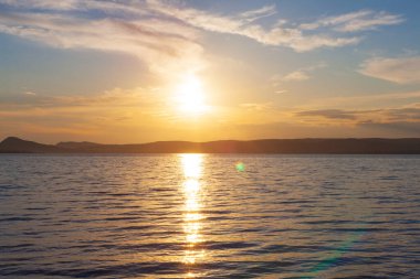 Yaz mevsiminde gün batımında göl üzerinde güneş ışıldar ve güneş suyun üzerinde parlar.