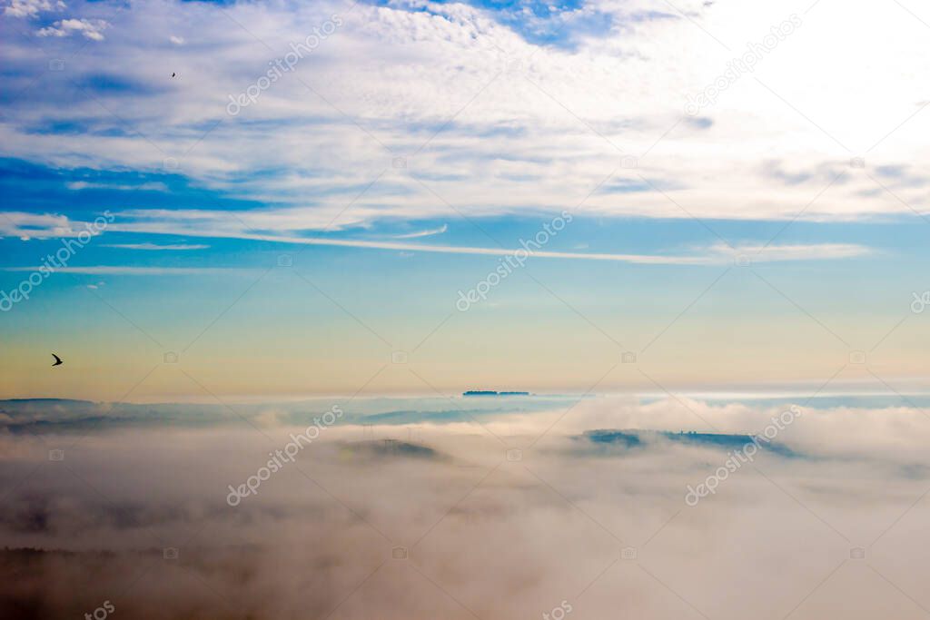 Summer landscape of early foggy morning over hills with bright blue sky and clouds. Thick fog over horizon in Siberia, Russia