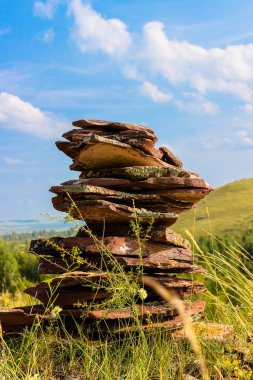 Yazın mavi gökyüzünün altındaki tepede bulunan Devonian kumtaşından yapılmış kırmızımsı dengeli taşların piramidi. Seçici odak