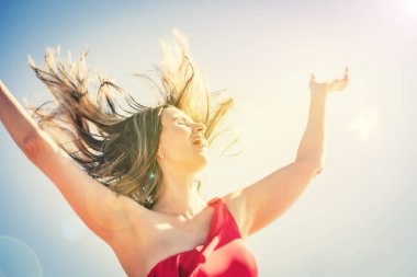 İnce, güzel bir Avrupalı orta yaşlı kadın gökyüzüne karşı kırmızı mayo giymiş olgun bir pantolonla dinlenmek için uçtu. Rüzgar onun uzun siyah saçlarını geliştirir.