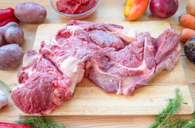 Tahta bir tahta, soğan, sarımsak, biber ve sebze yağının üzerine işlenmemiş bir kemik parçası uzanır. Biftek yakın plan. Taze koyun eti. Yukarıdan görünüşü.