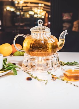 Kokulu taze bitki çayı ve cam çaydanlıkta ısınan Melissa beyaz bir masada. Geleneksel bitkisel içecek. Lokantada ballı çay. Su ısıtıcı.