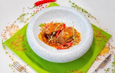 Yeşil bir masa örtüsü üzerinde mermer gri bir tabakta hecelenmiş sığır eti yanakları. Dekor