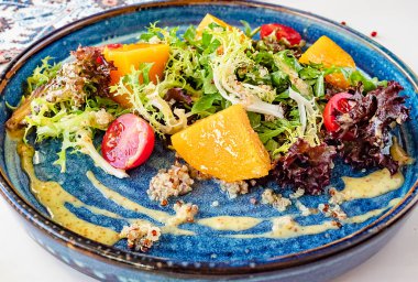 Fırında balkabağı, kiraz domatesli salata ve mavi seramik tabakta otlar.