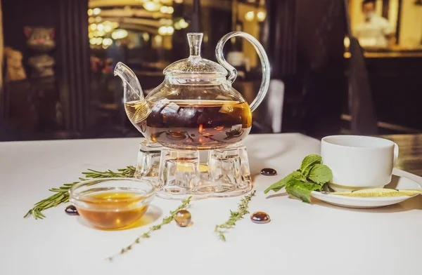 蜂蜜と新鮮なミントの葉と暖かいぼやけた背景を持つガラスティーポットの芳香族ホット緑茶 カフェでお茶と一緒にテーブルを提供します ケトル暖かい — ストック写真