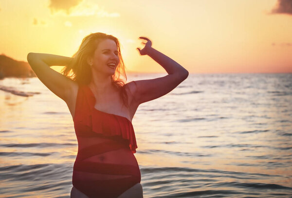 carefree woman in red swimsuit dancing at sunset on the beach. mature woman relaxation vitality healthy lifestyle. Copy space